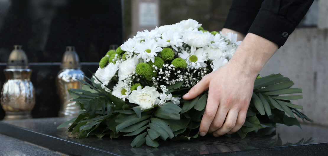 Kobieta kładzie białe kwiaty na grobie na cmentarzu, spokojna chwila pożegnania.